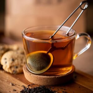 Warm glass cup of freshly brewed tea with a tea infuser and cookies on a wooden surface.